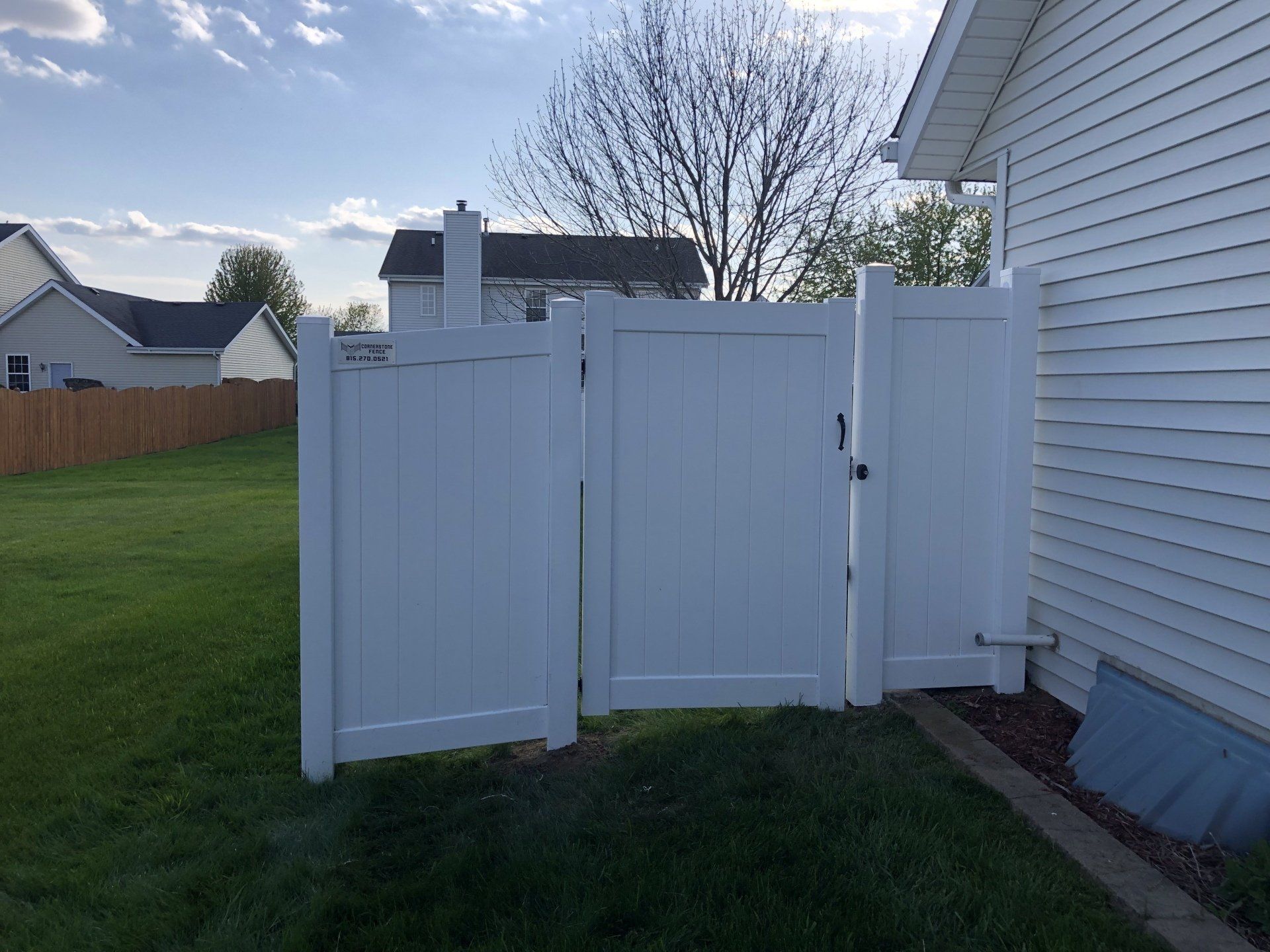 A white fence with a gate in the backyard of a house.