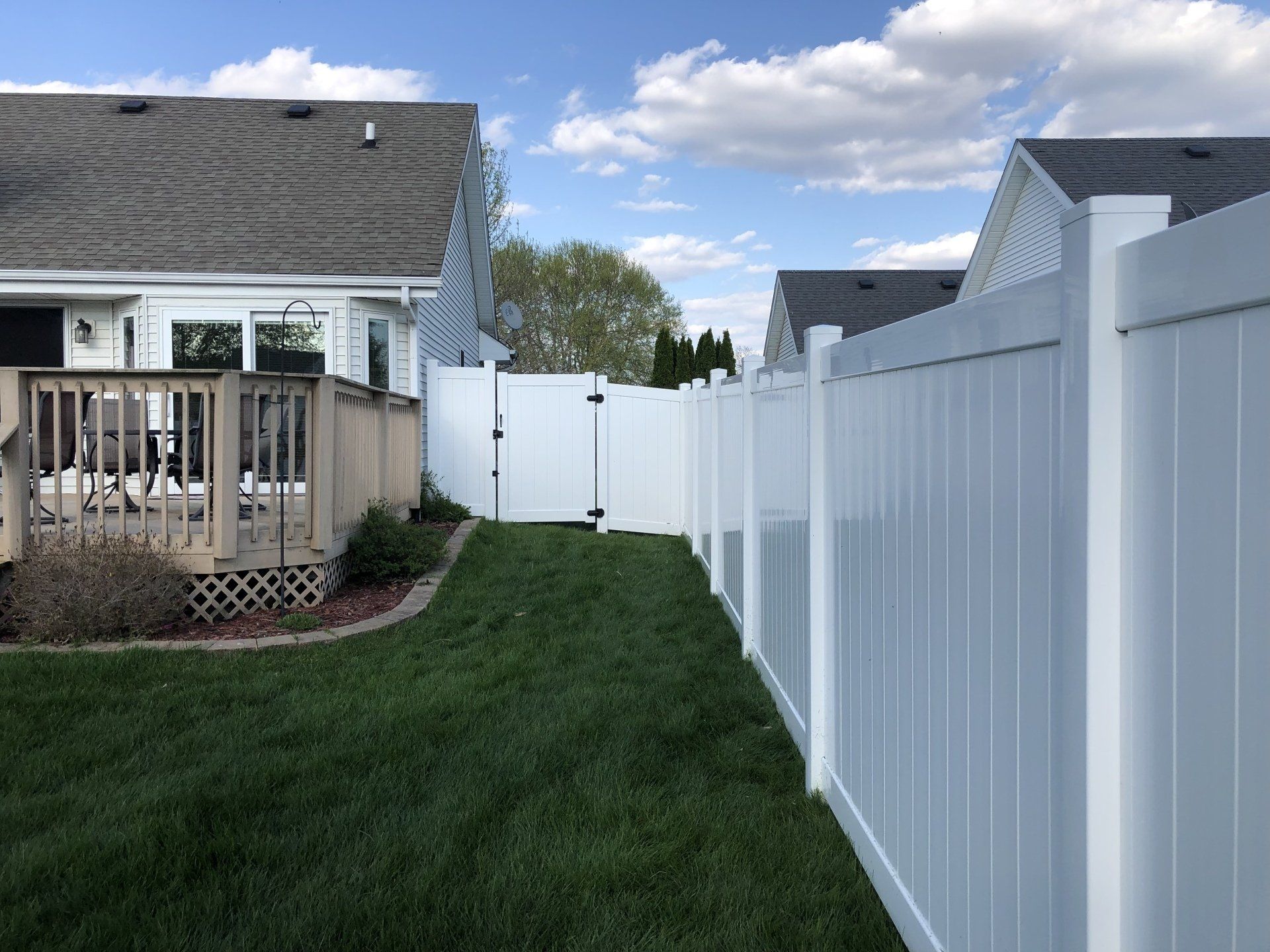A white fence surrounds a lush green yard in front of a house.