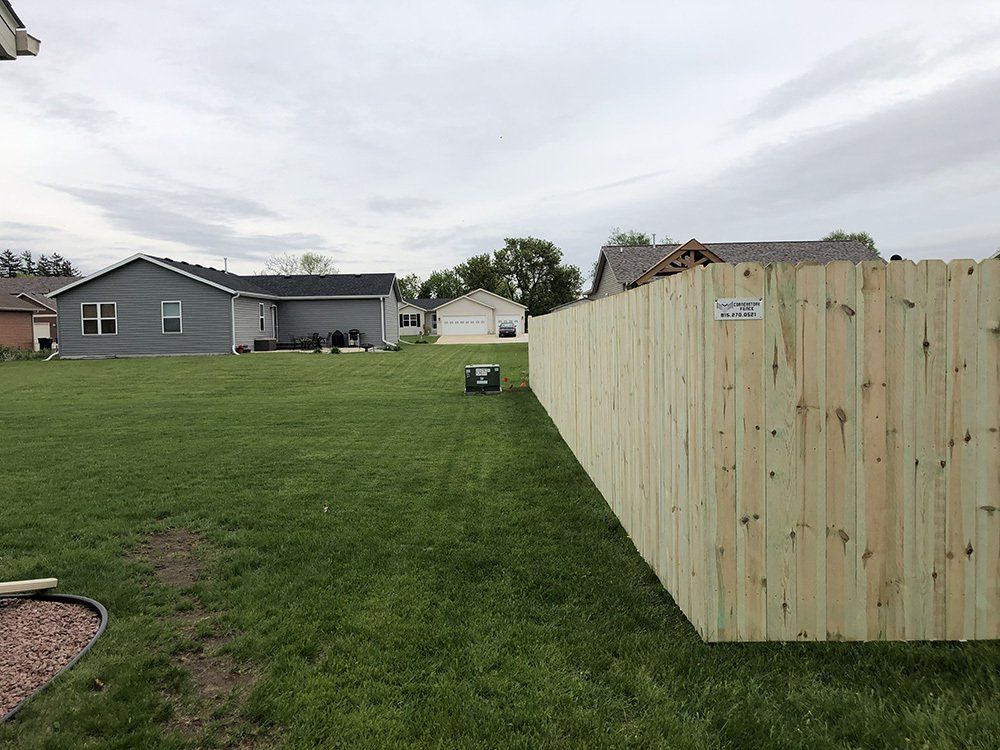 A wooden fence surrounds a lush green yard in front of a house.
