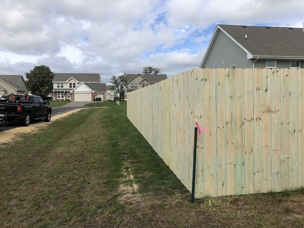 A wooden fence is sitting in the middle of a grassy field next to a house.