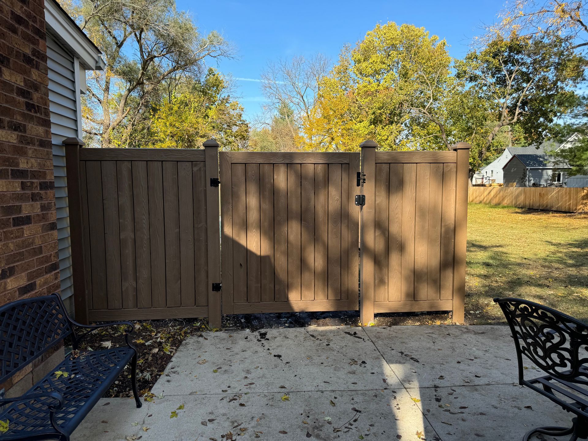 A wooden fence is surrounding a patio with a bench and chairs.