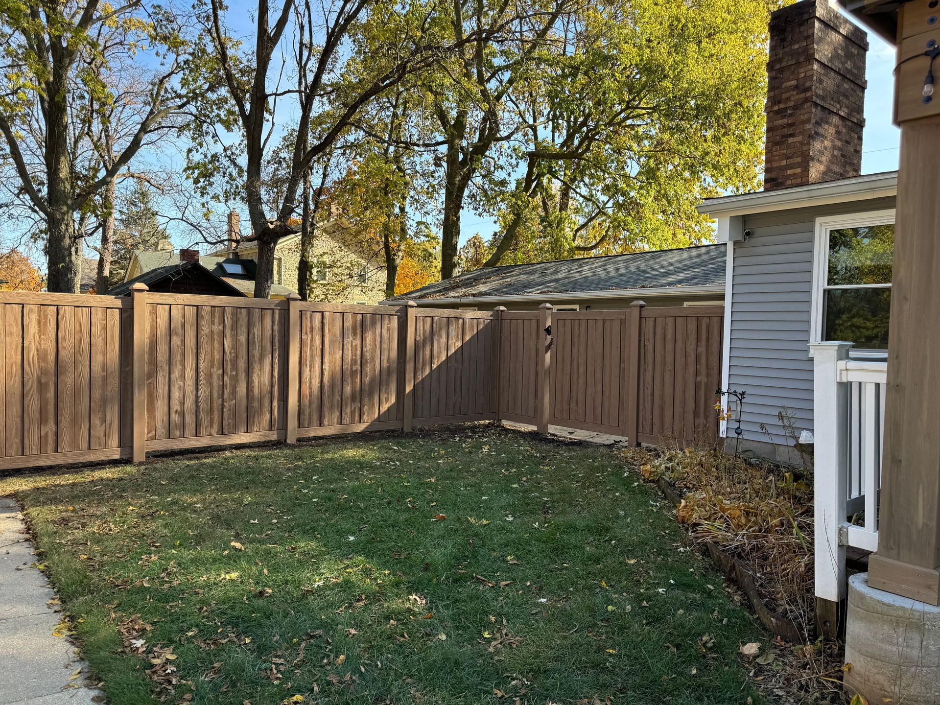 A wooden fence surrounds a lush green yard in front of a house.