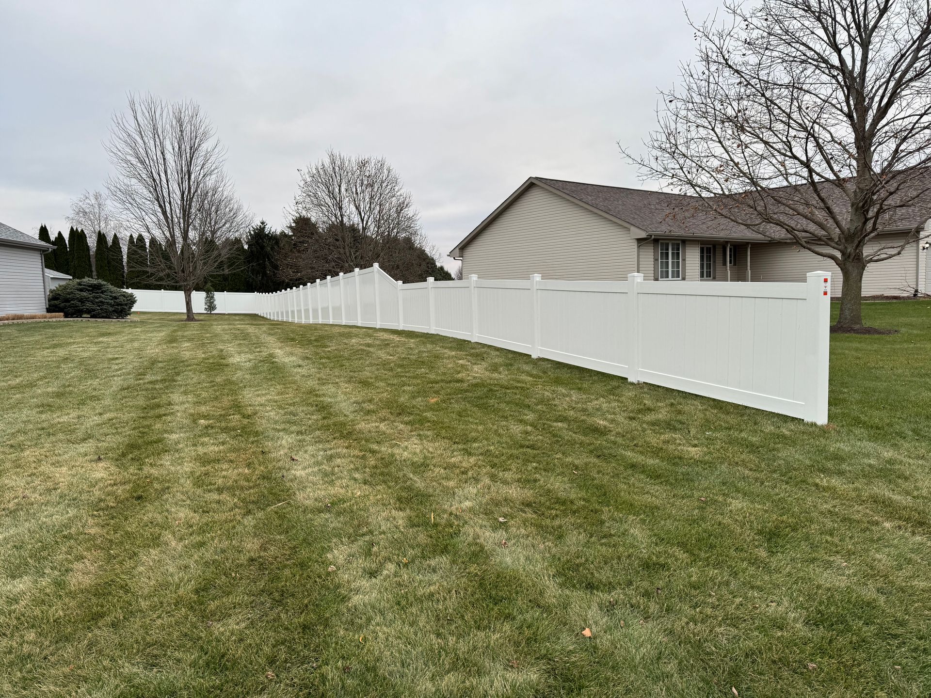 A white fence surrounds a lush green lawn in front of a house.