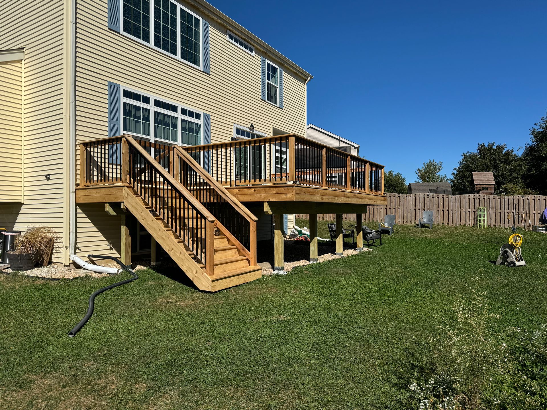 A large wooden deck with stairs is in the backyard of a house.