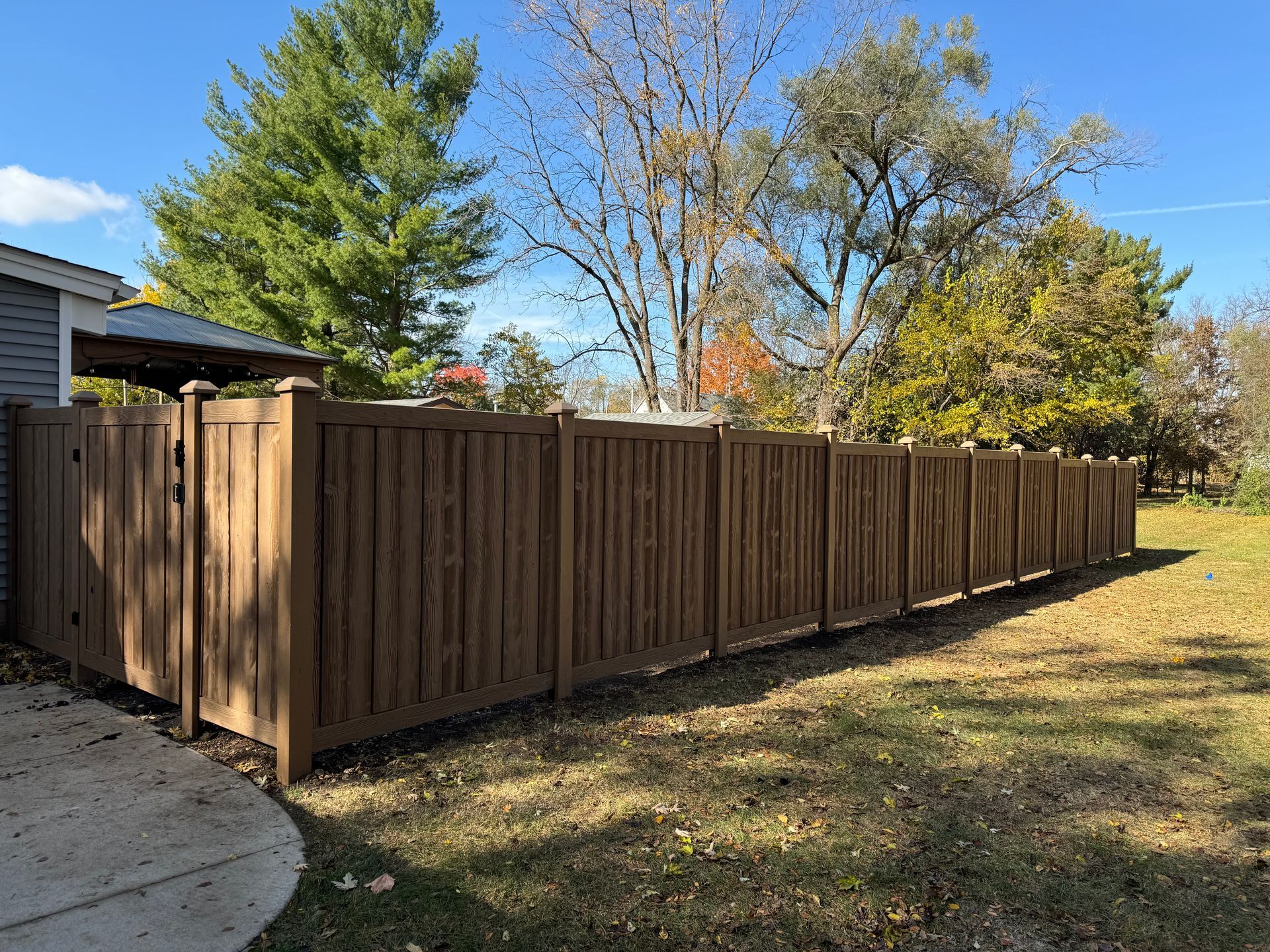 A wooden fence surrounds a lush green field in front of a house.