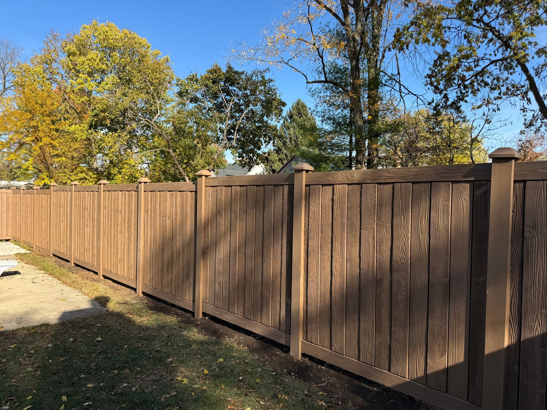 A wooden fence surrounds a backyard with trees in the background.