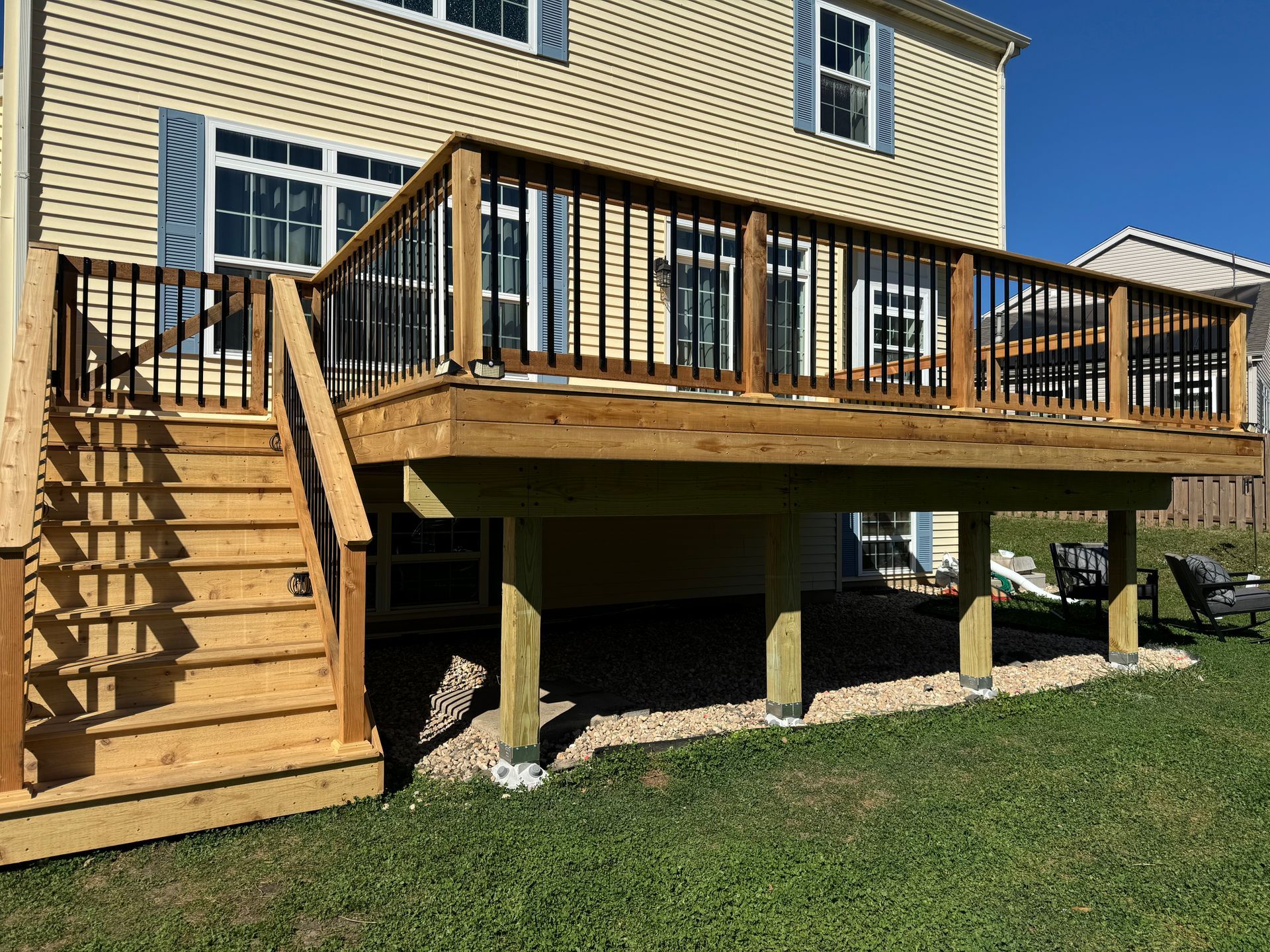 A large wooden deck with stairs leading up to it is in the backyard of a house.