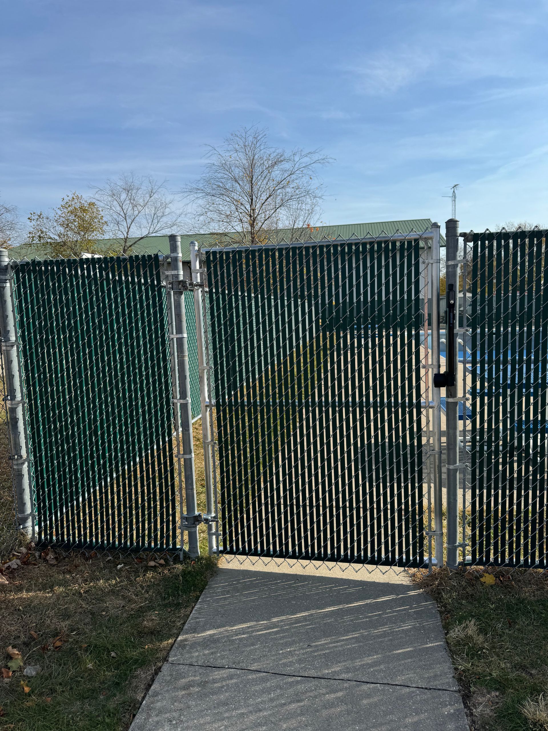 A fence with a green slat covering is surrounding a walkway.