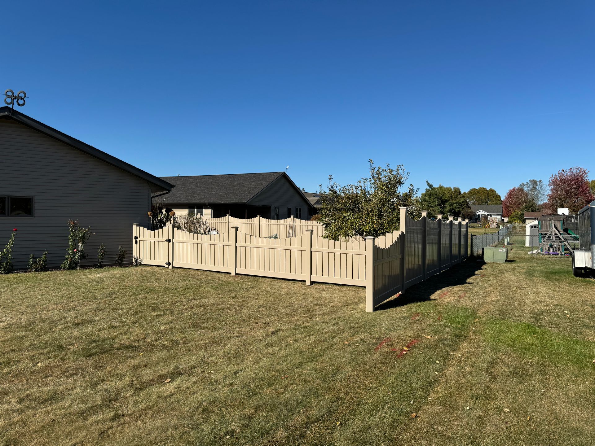A wooden fence surrounds a grassy yard in front of a house.