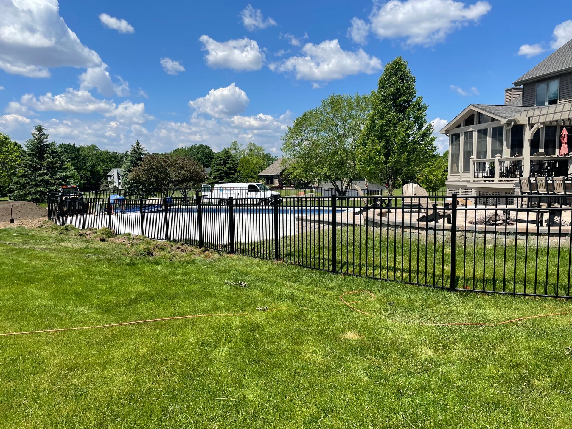 There is a large house in the background and a pool in the backyard behind the fence.