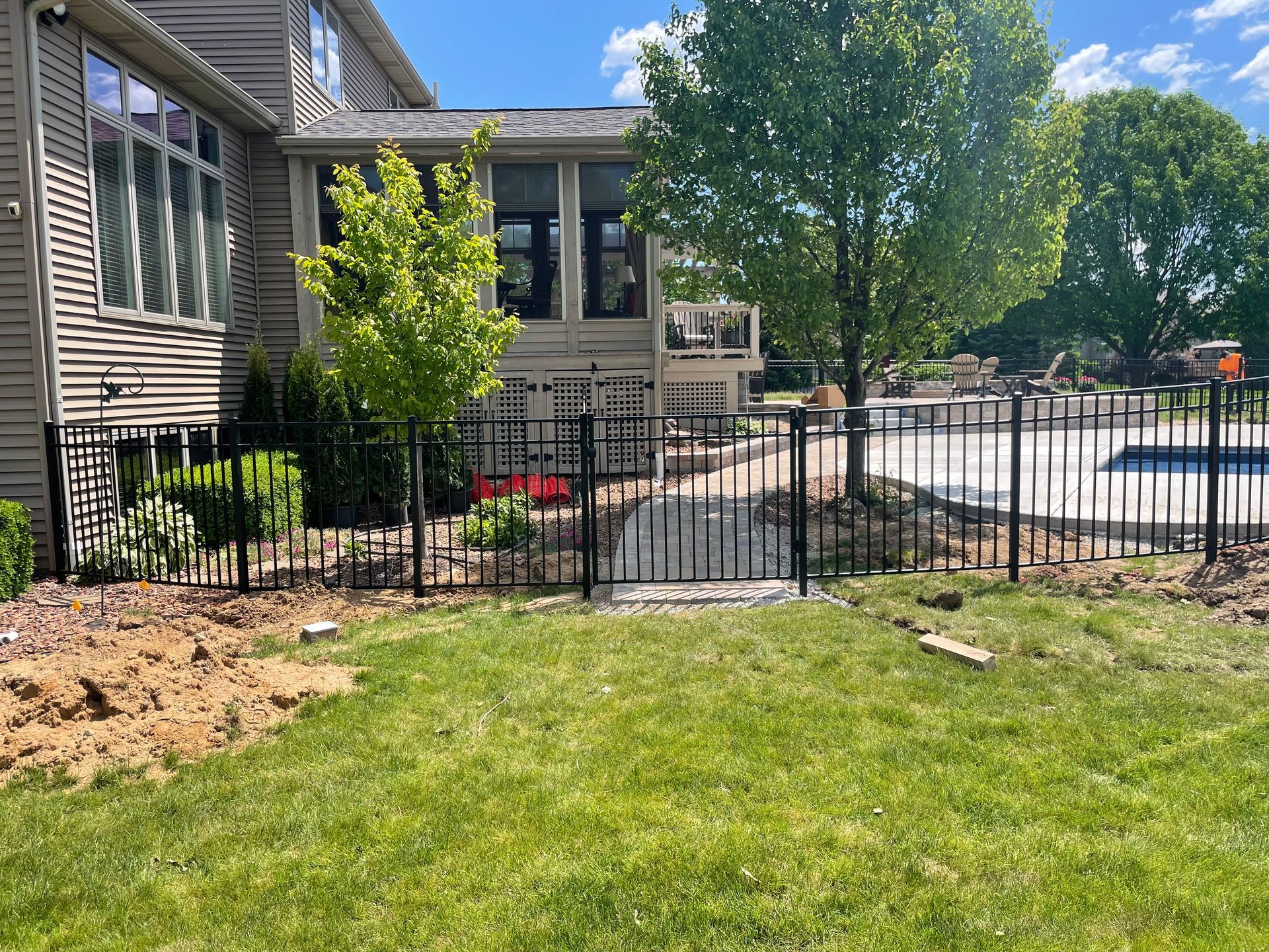 A metal fence surrounds a lush green lawn in front of a house.