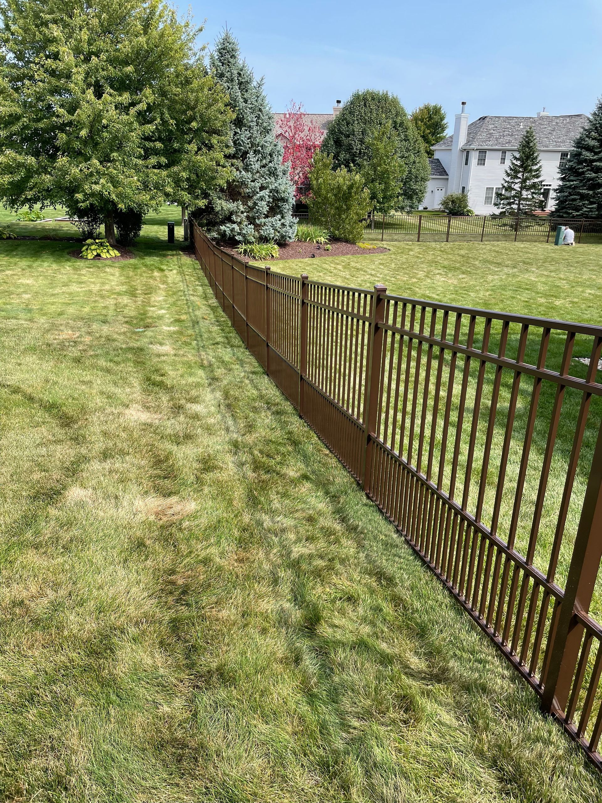 A metal fence surrounds a lush green lawn in a backyard.