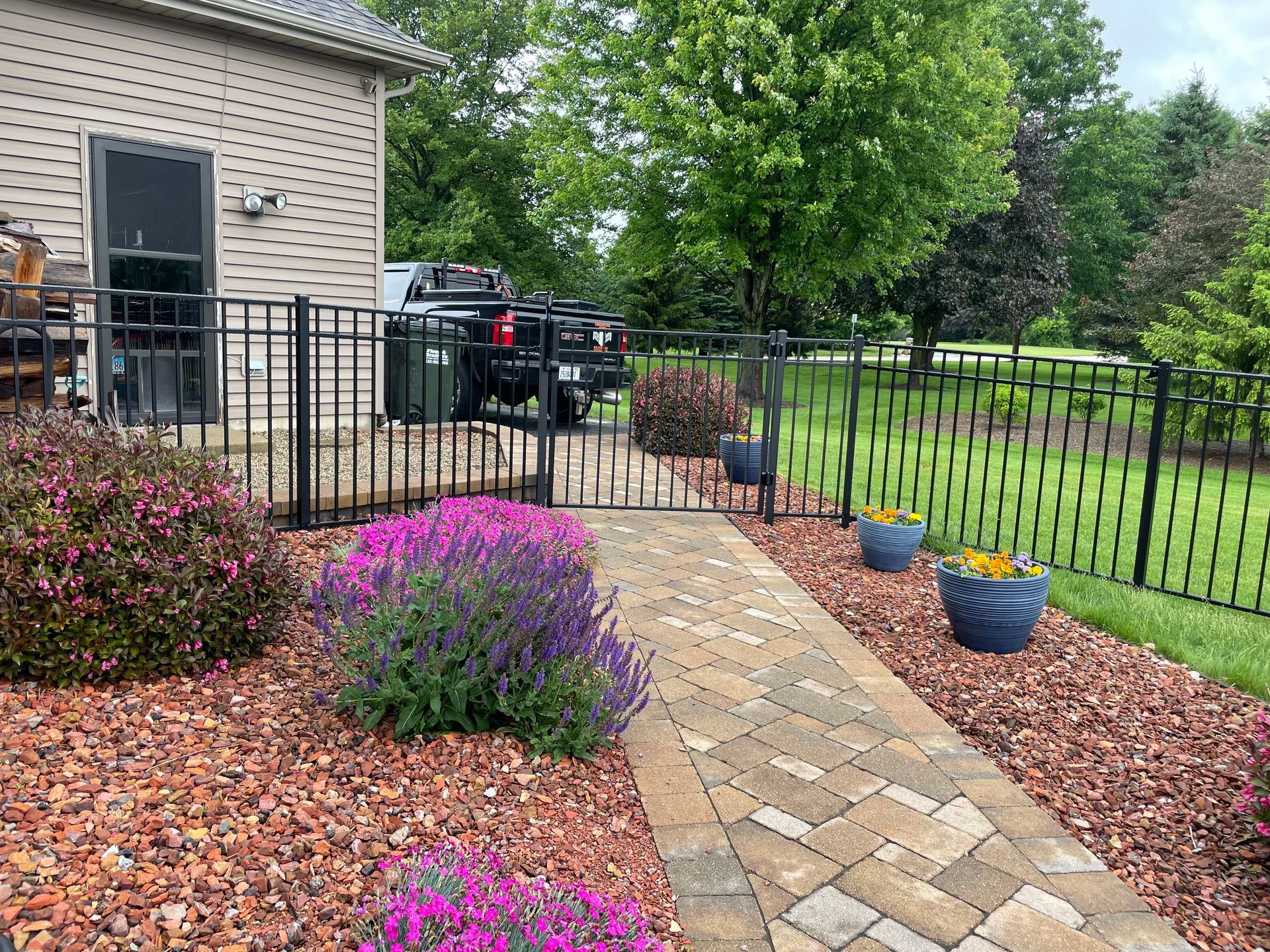 A brick walkway leading to a house with a fence and flowers.