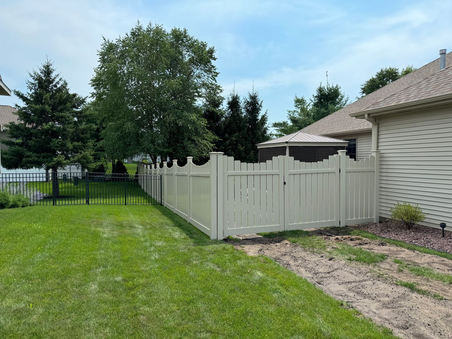 A white fence is in the backyard of a house.