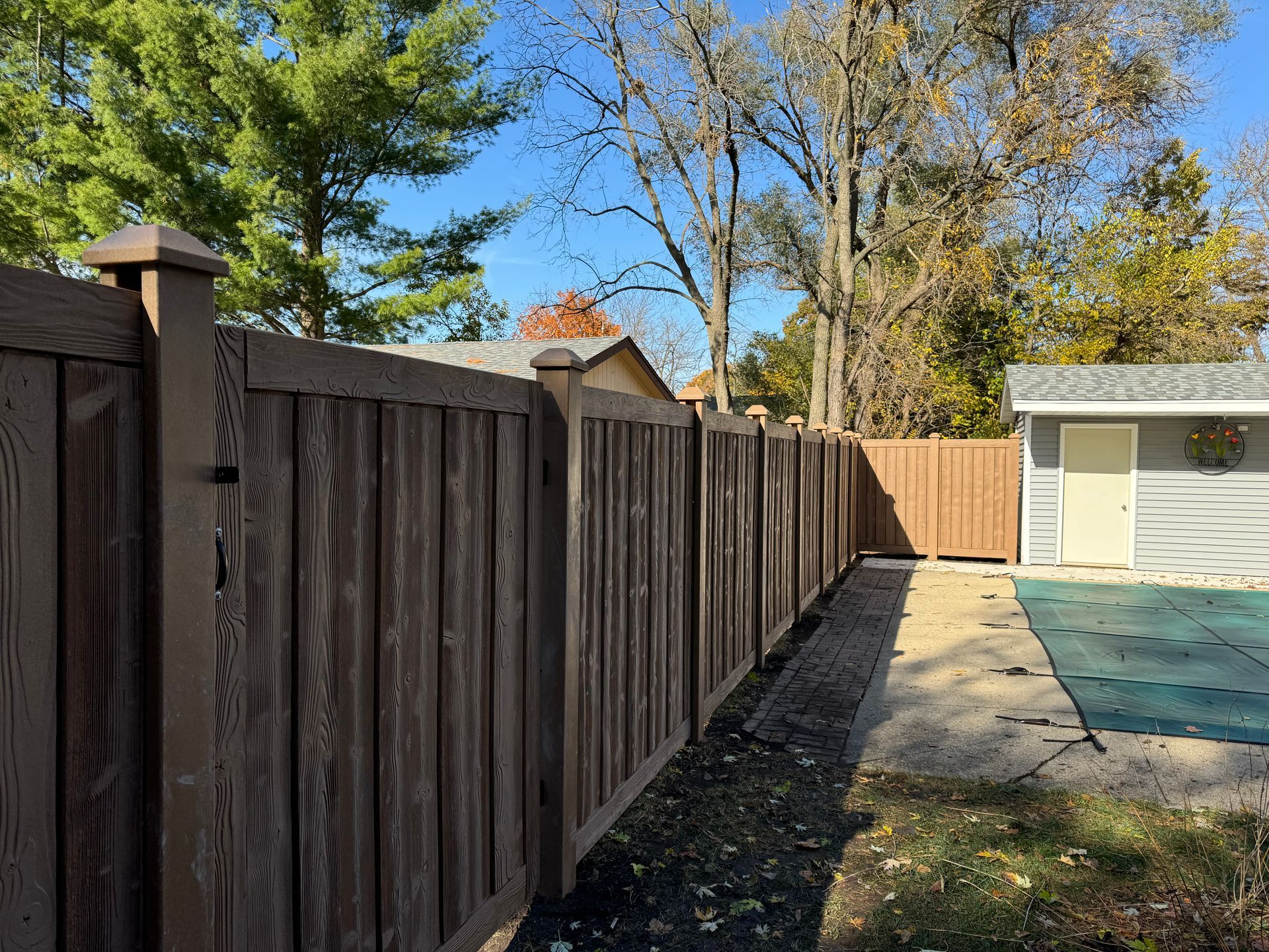 A wooden fence surrounds a swimming pool in a backyard.