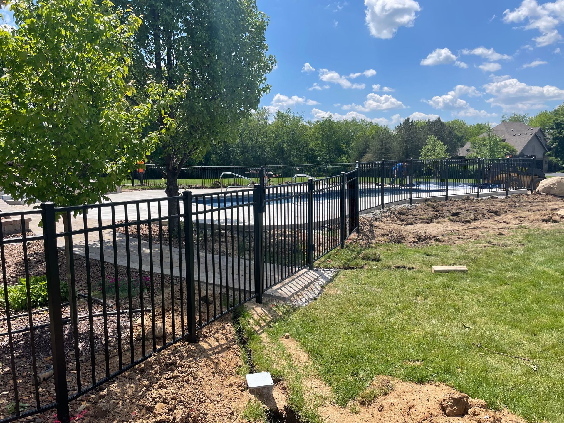 A black metal fence surrounds a swimming pool in a backyard.