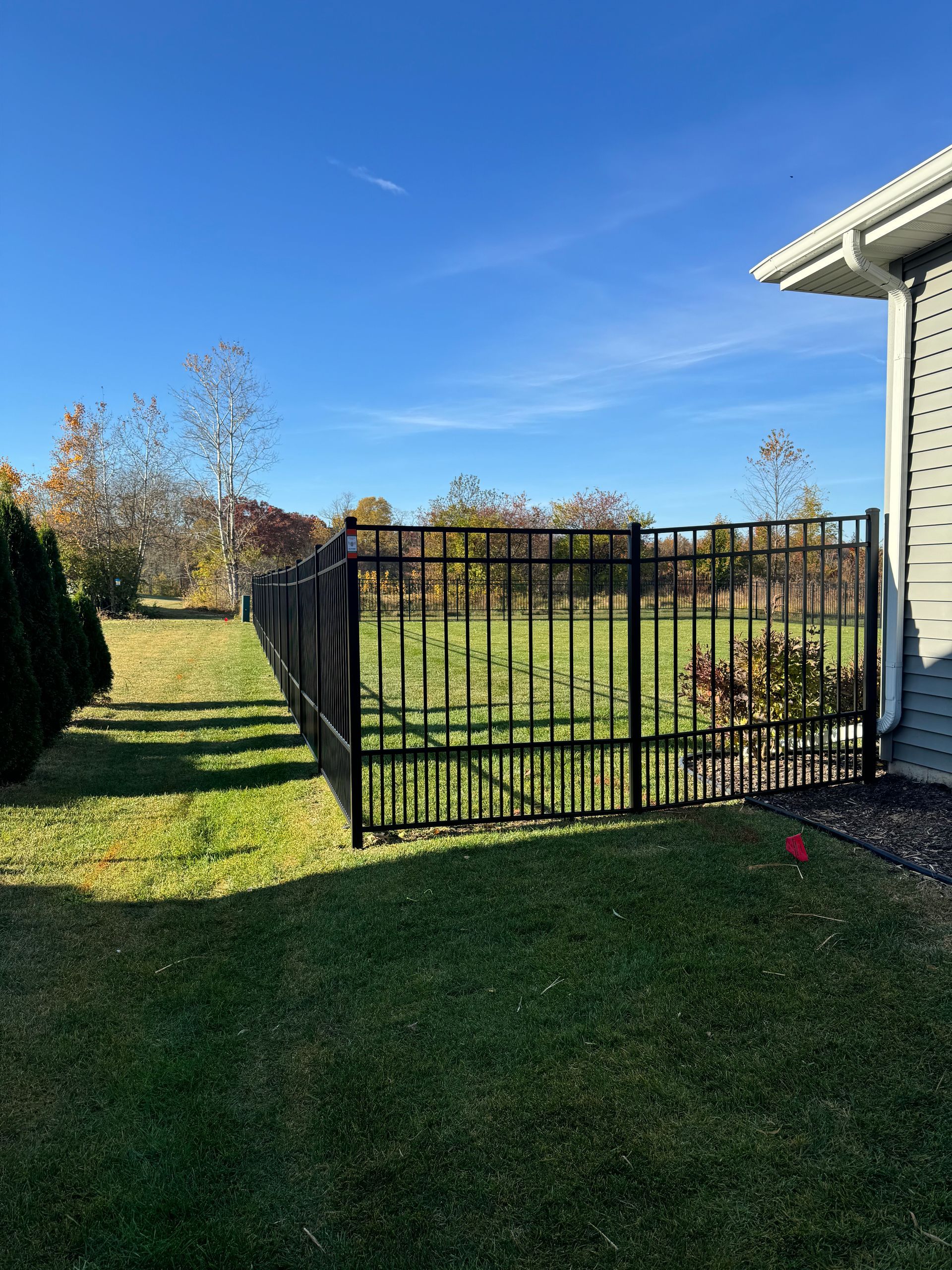 A black fence surrounds a lush green field in front of a house.