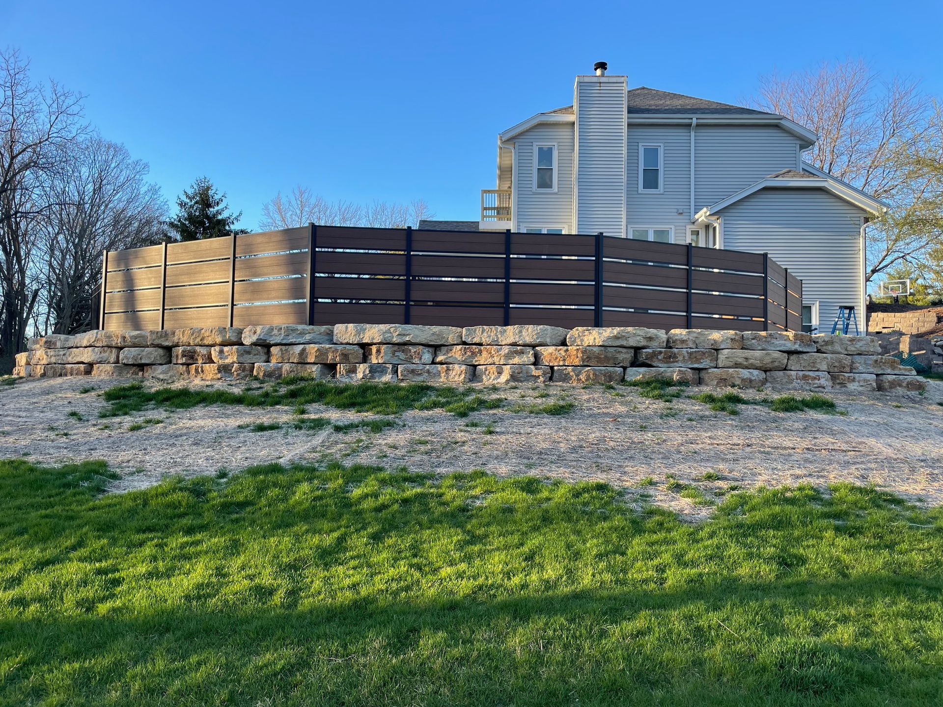 A house with a wooden fence and a stone wall in front of it.