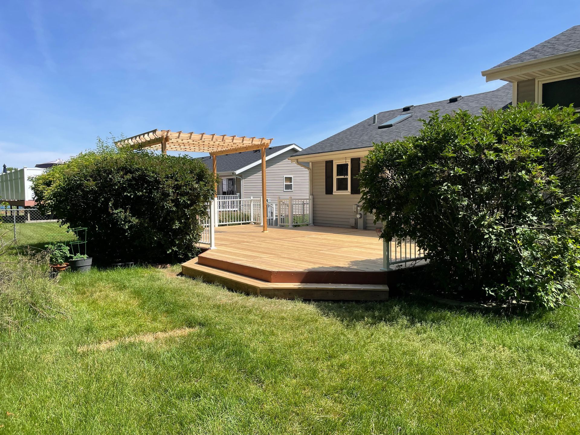 A wooden deck with a pergola in the backyard of a house.