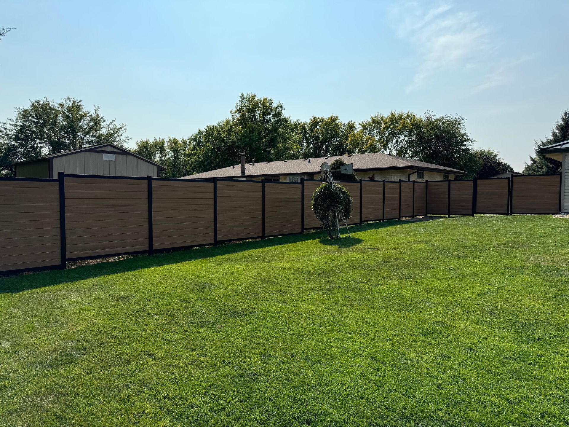 A wooden fence surrounds a lush green lawn in a backyard.