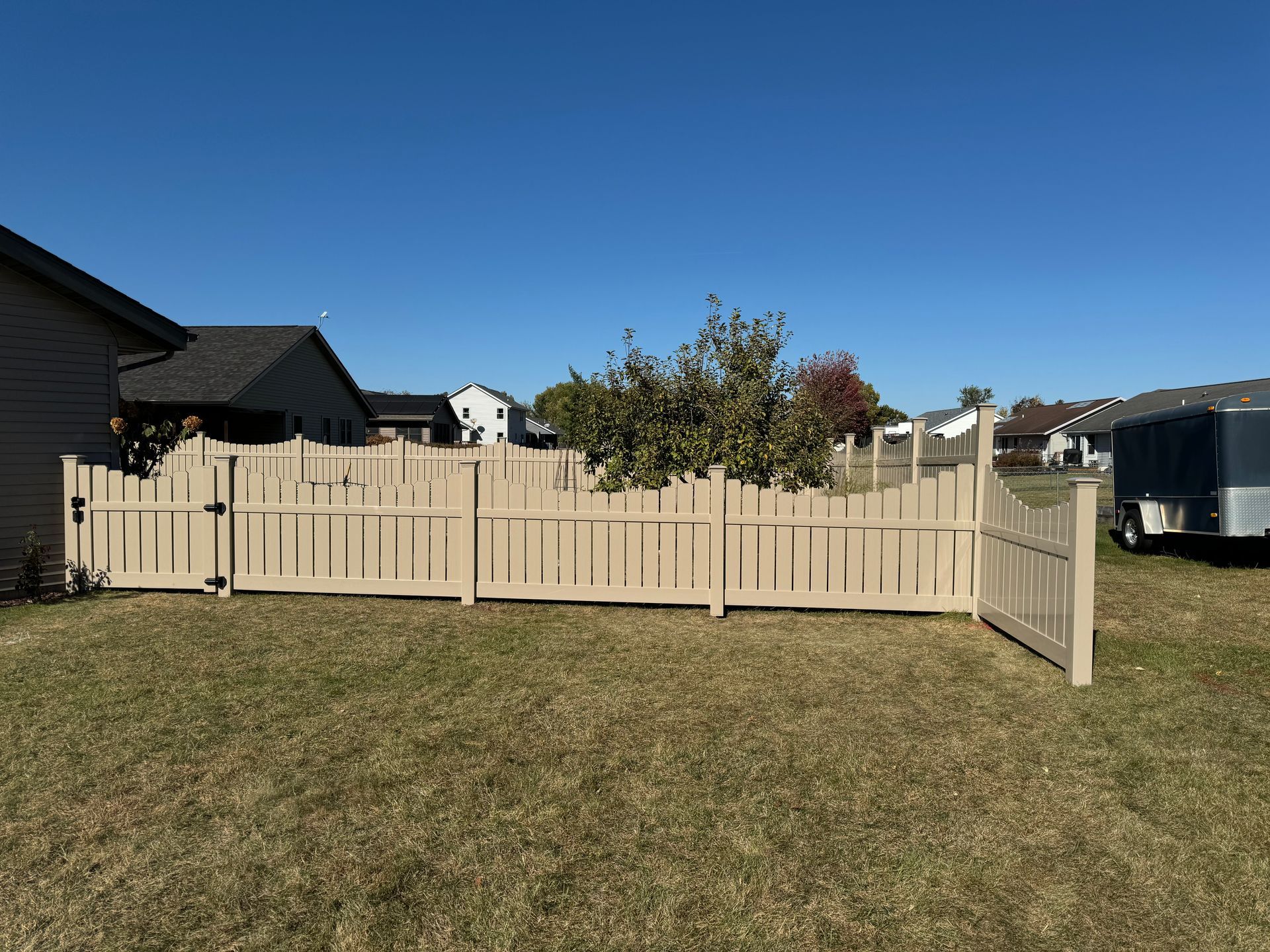 A wooden fence is in the middle of a grassy field in front of a house.