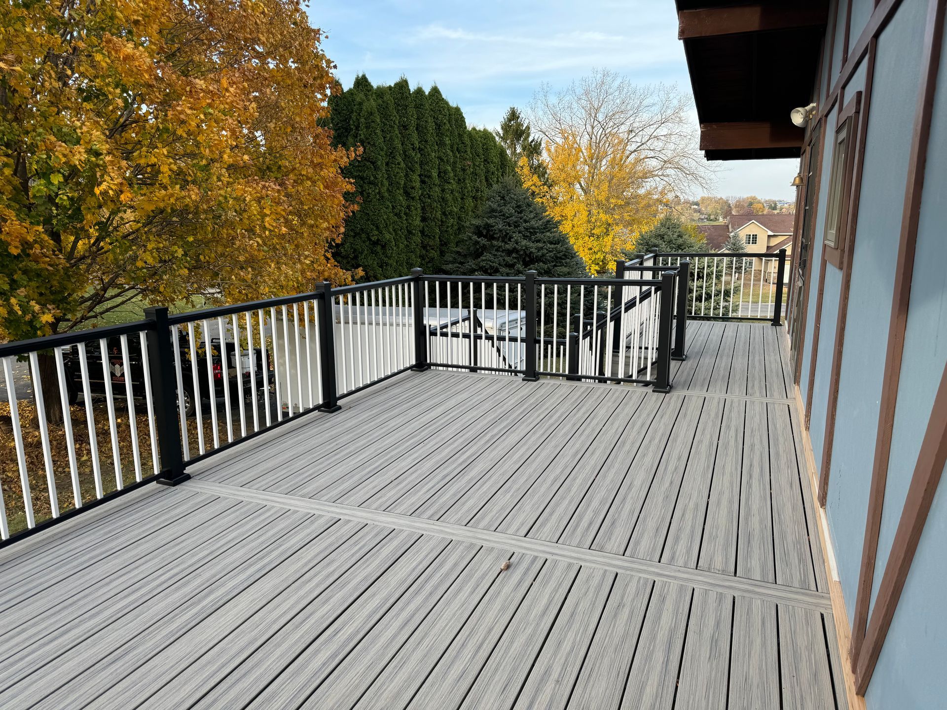 A large wooden deck with a black railing and trees in the background.