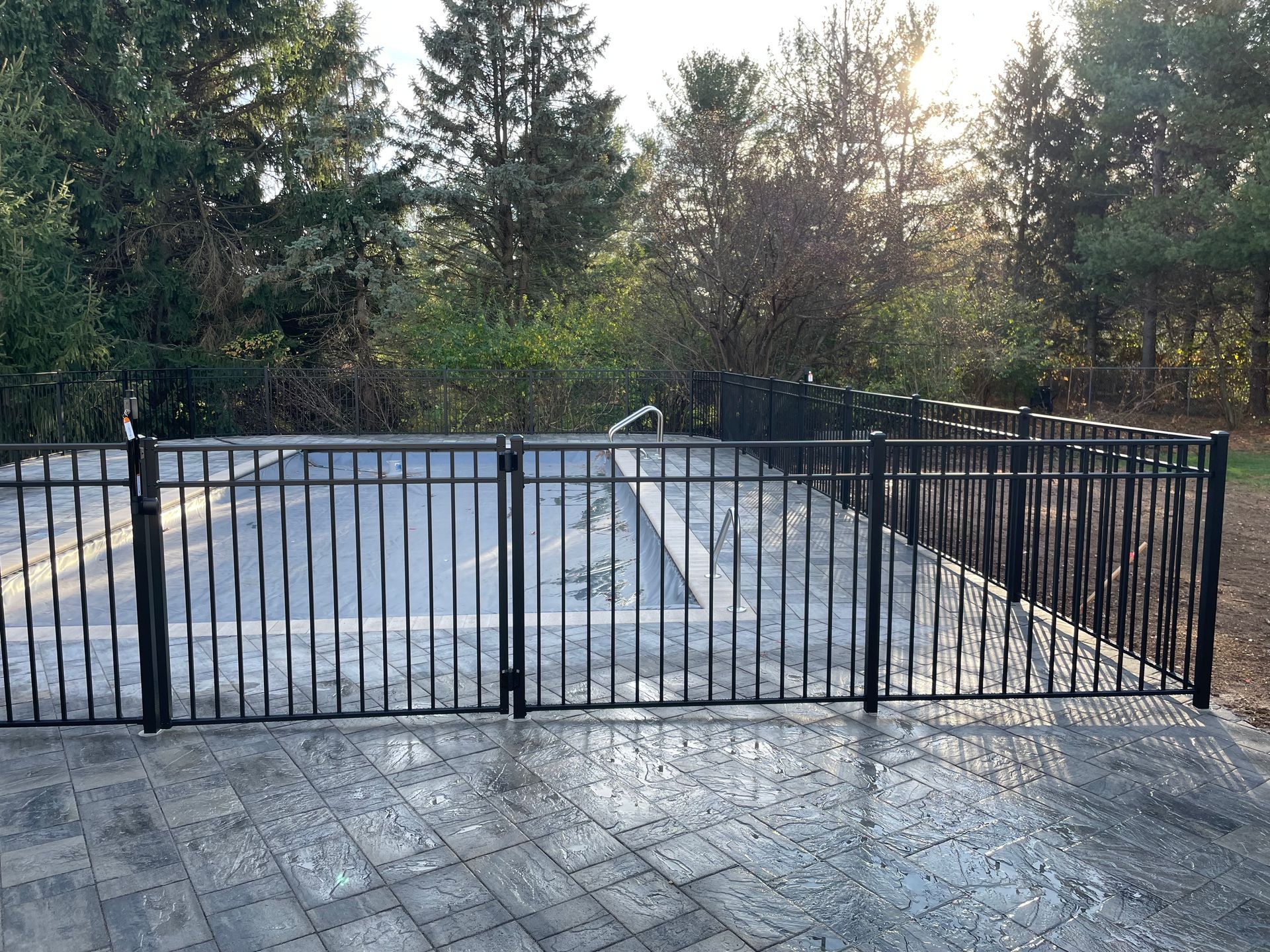 A black fence surrounds a swimming pool with trees in the background