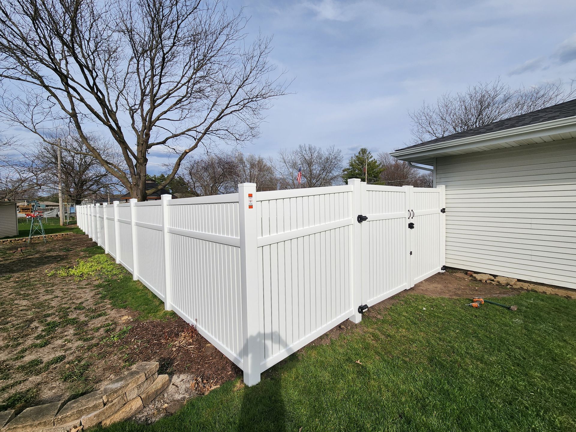 A white fence with a gate is in the backyard of a house.