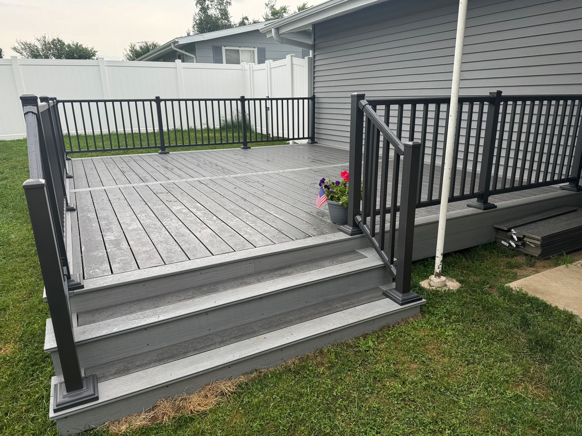 A gray deck with stairs and a black railing in front of a house.