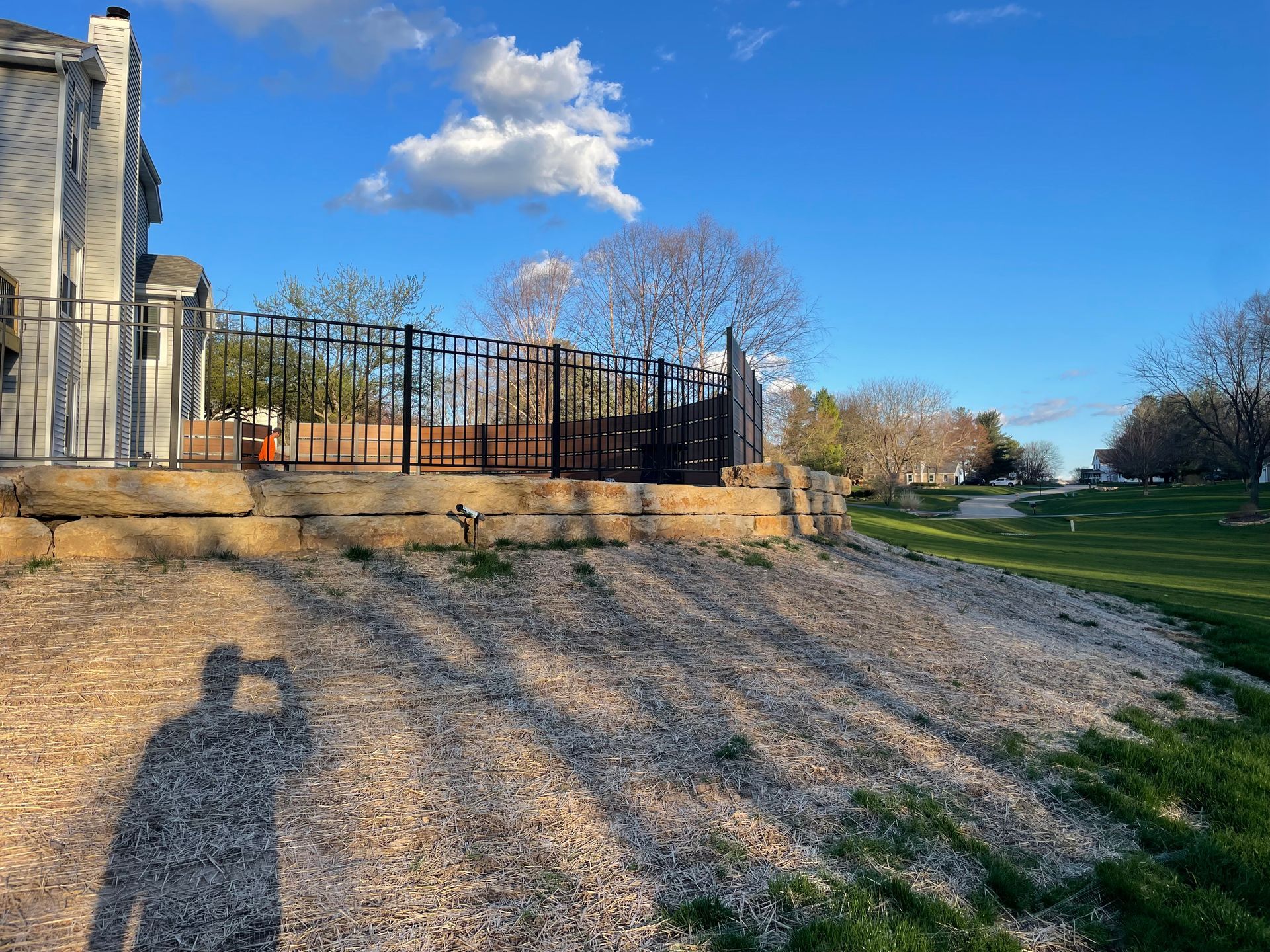 A shadow of a person is cast on a gravel road in front of a house.