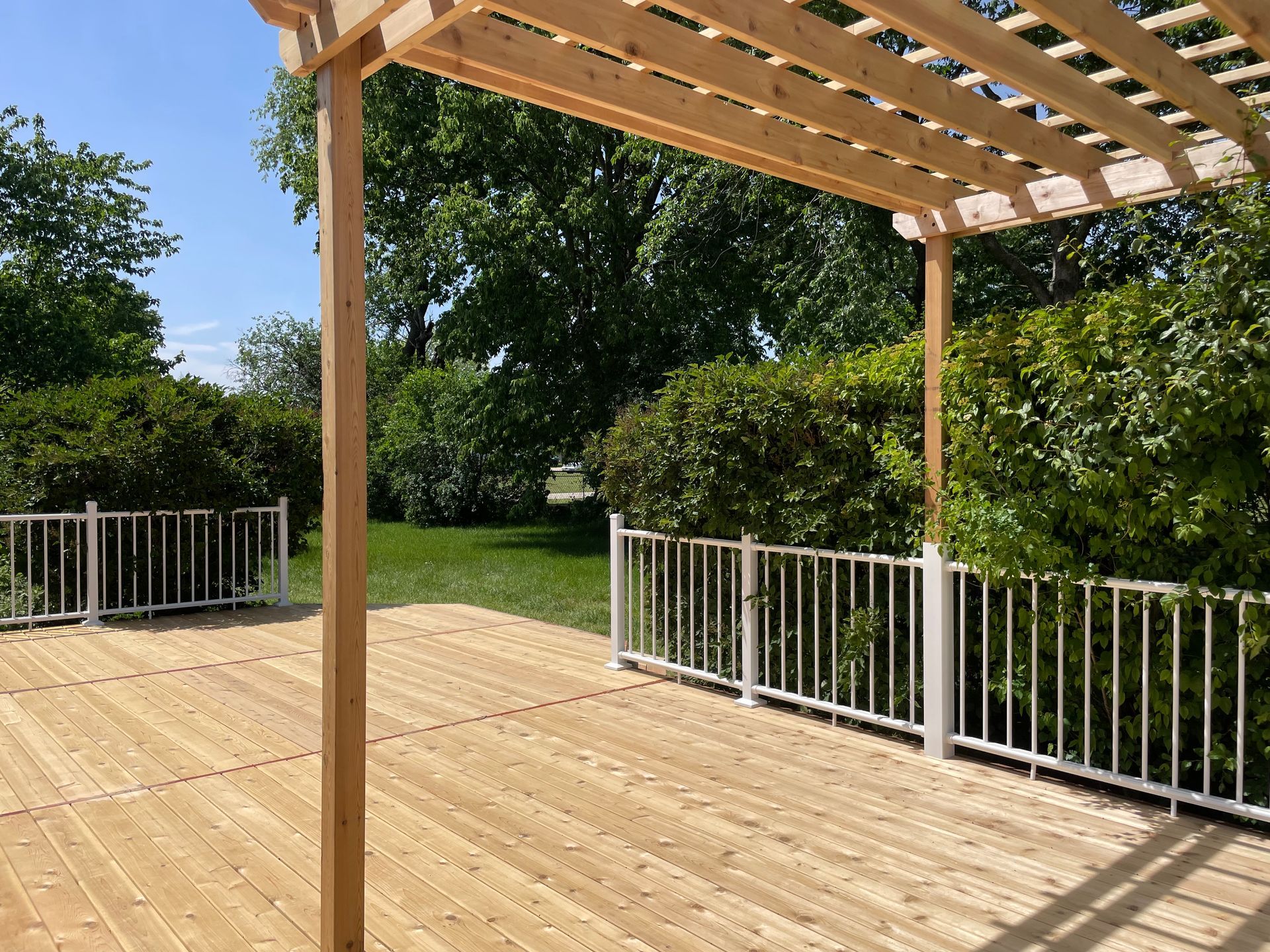 A wooden deck with a pergola and a white railing.