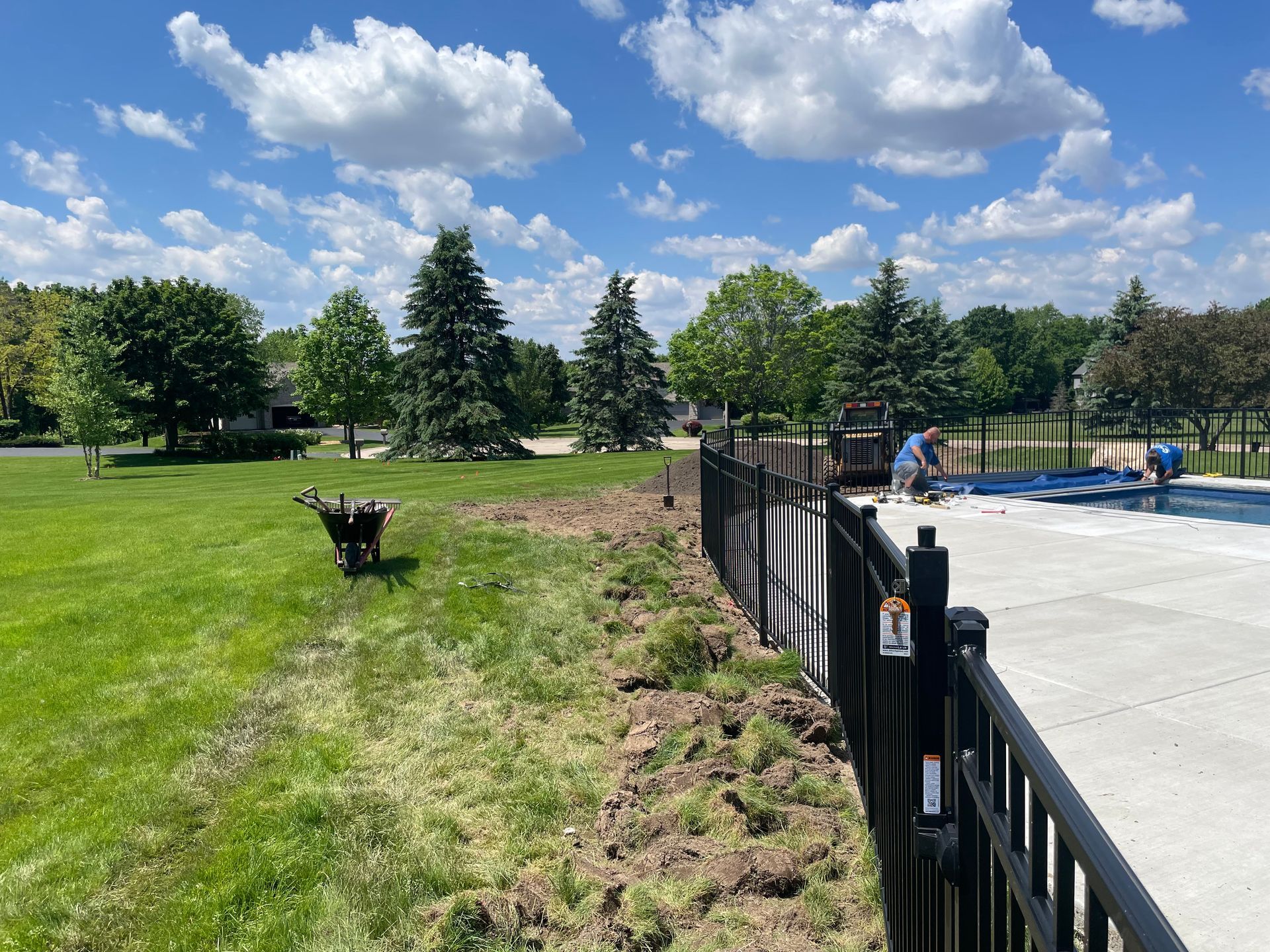 A black fence surrounds a lush green field next to a swimming pool.