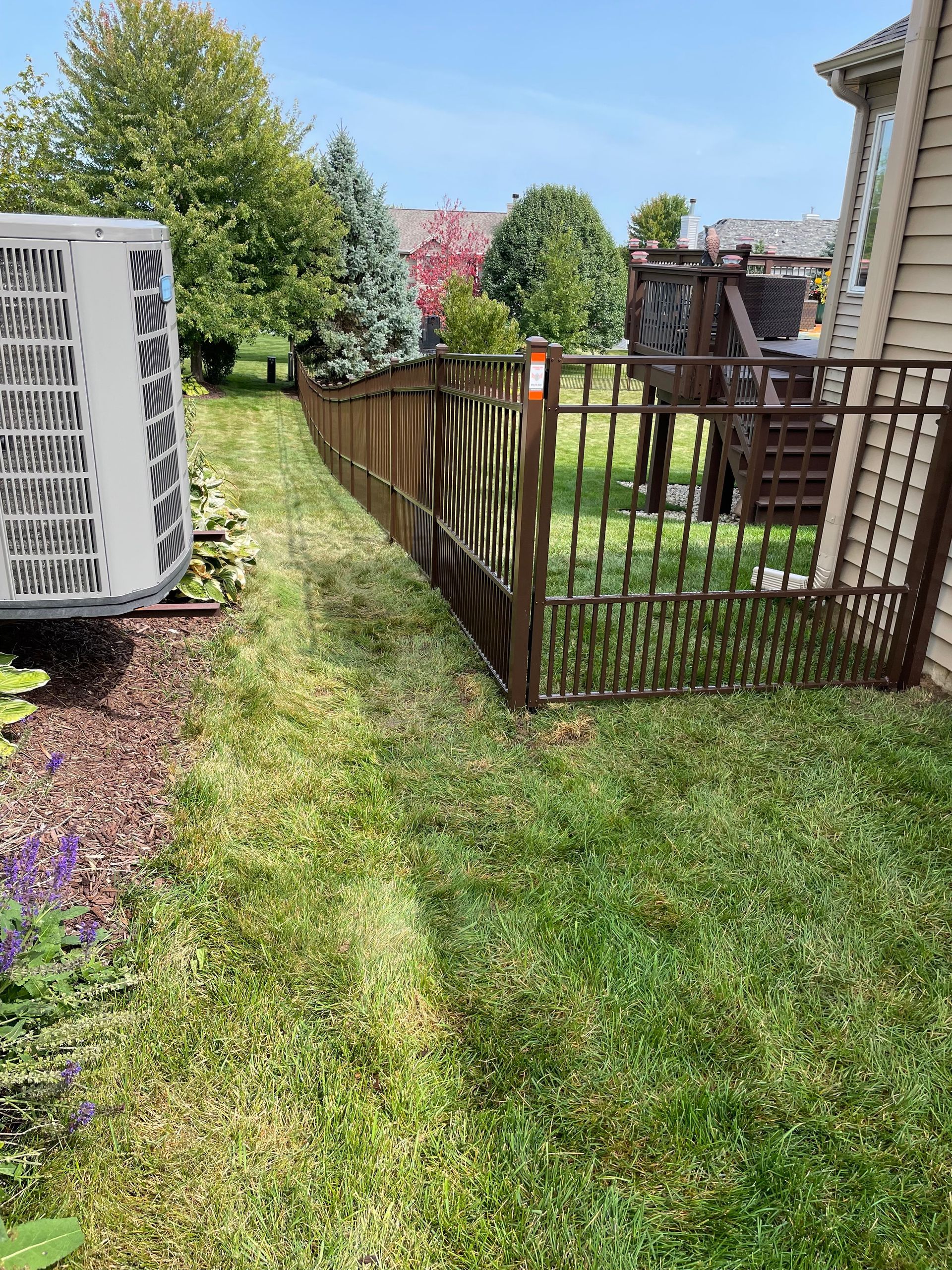 An air conditioner is sitting in the grass next to a fence.