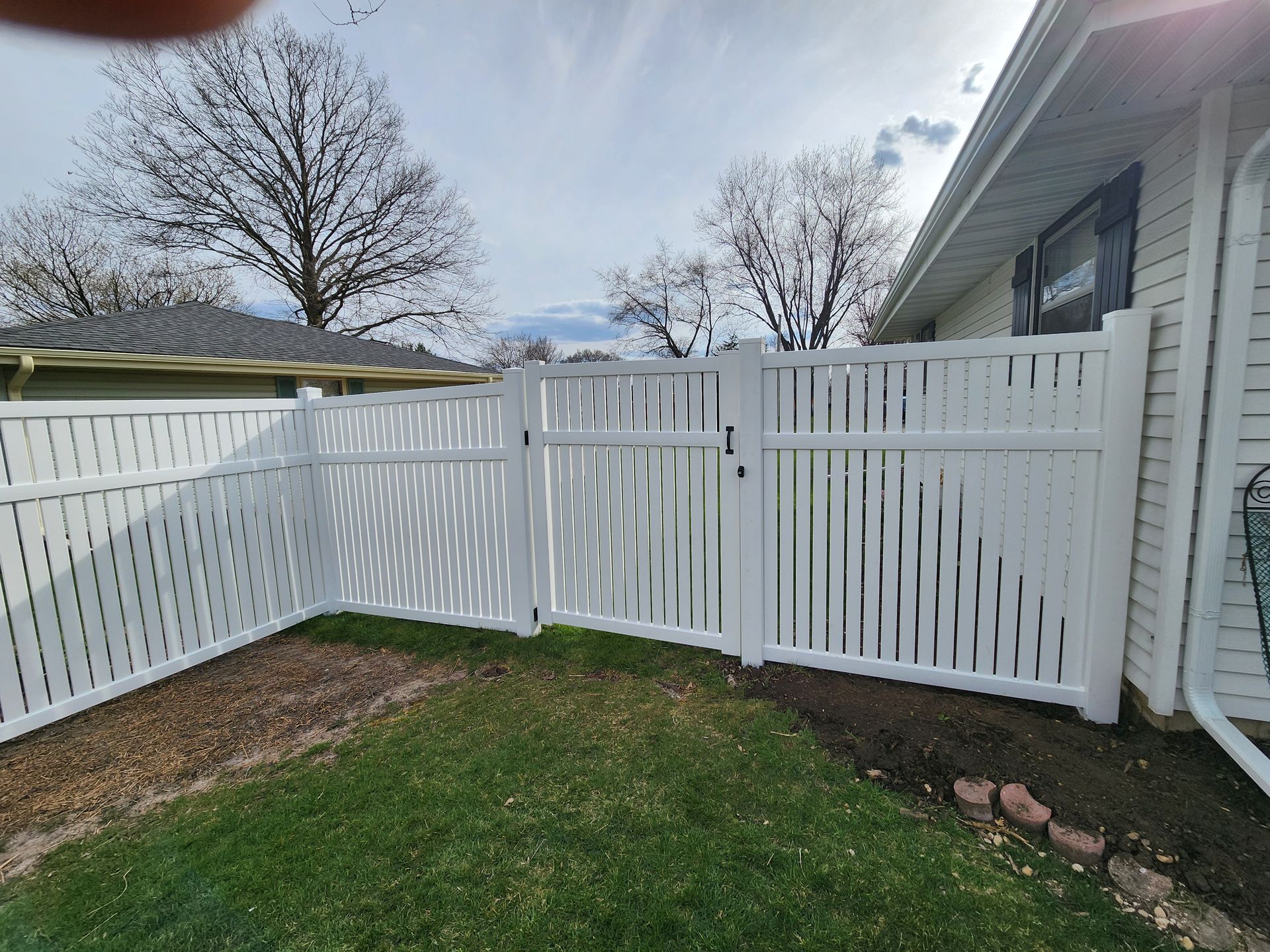 A white fence with a gate in the backyard of a house.
