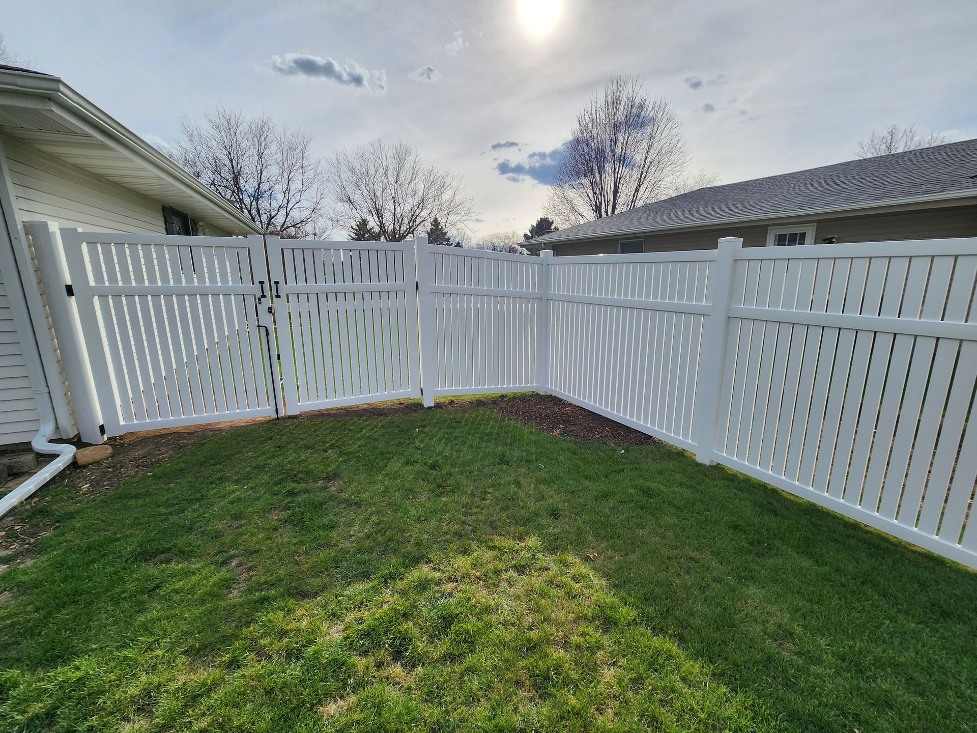 A white fence is in the backyard of a house.