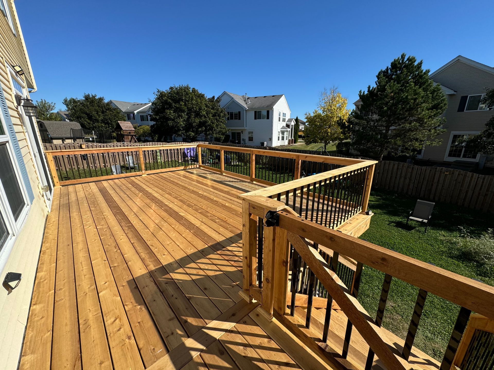 A large wooden deck with a metal railing and stairs leading up to it.