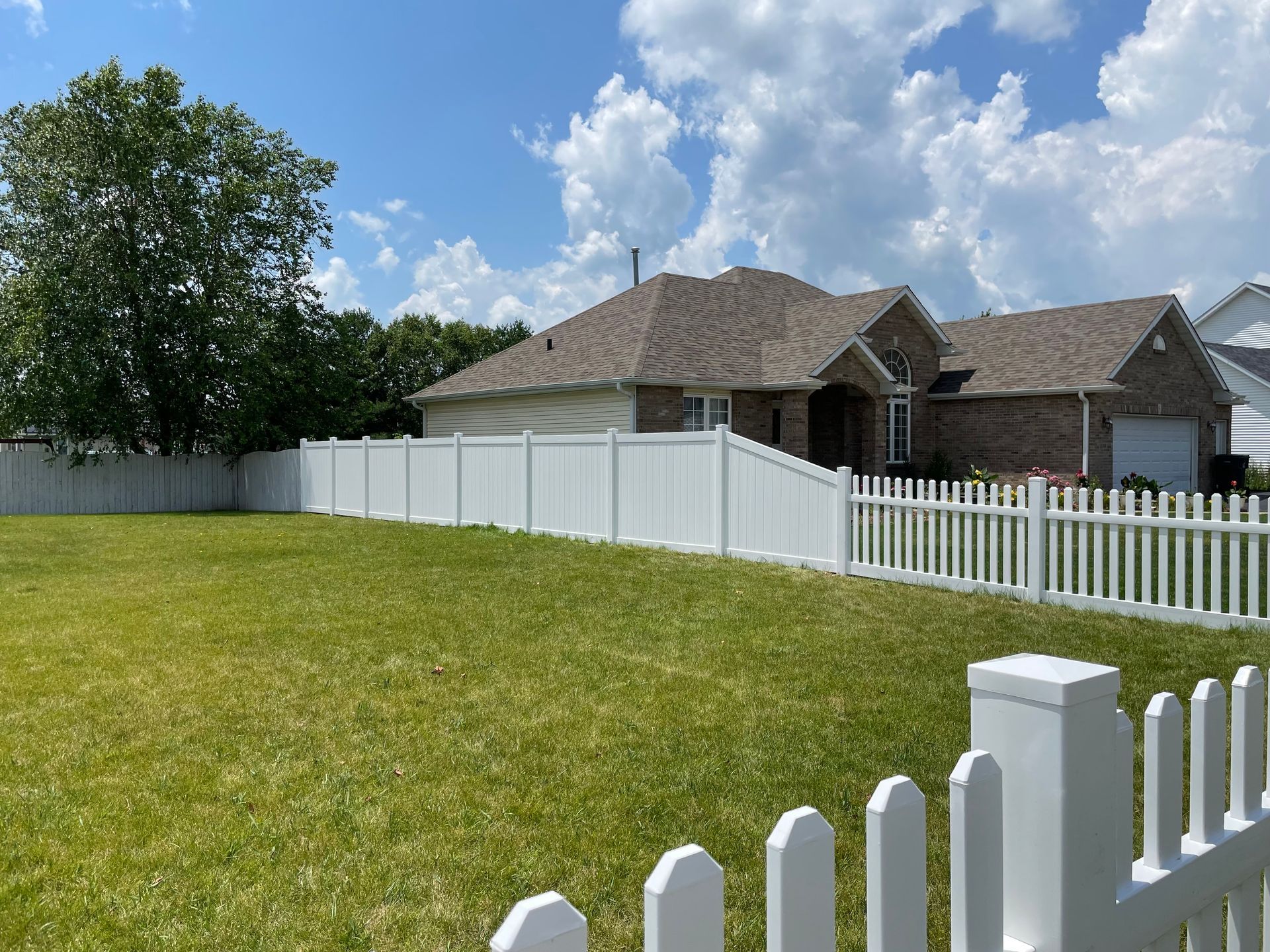 A white picket fence surrounds a lush green yard in front of a house.