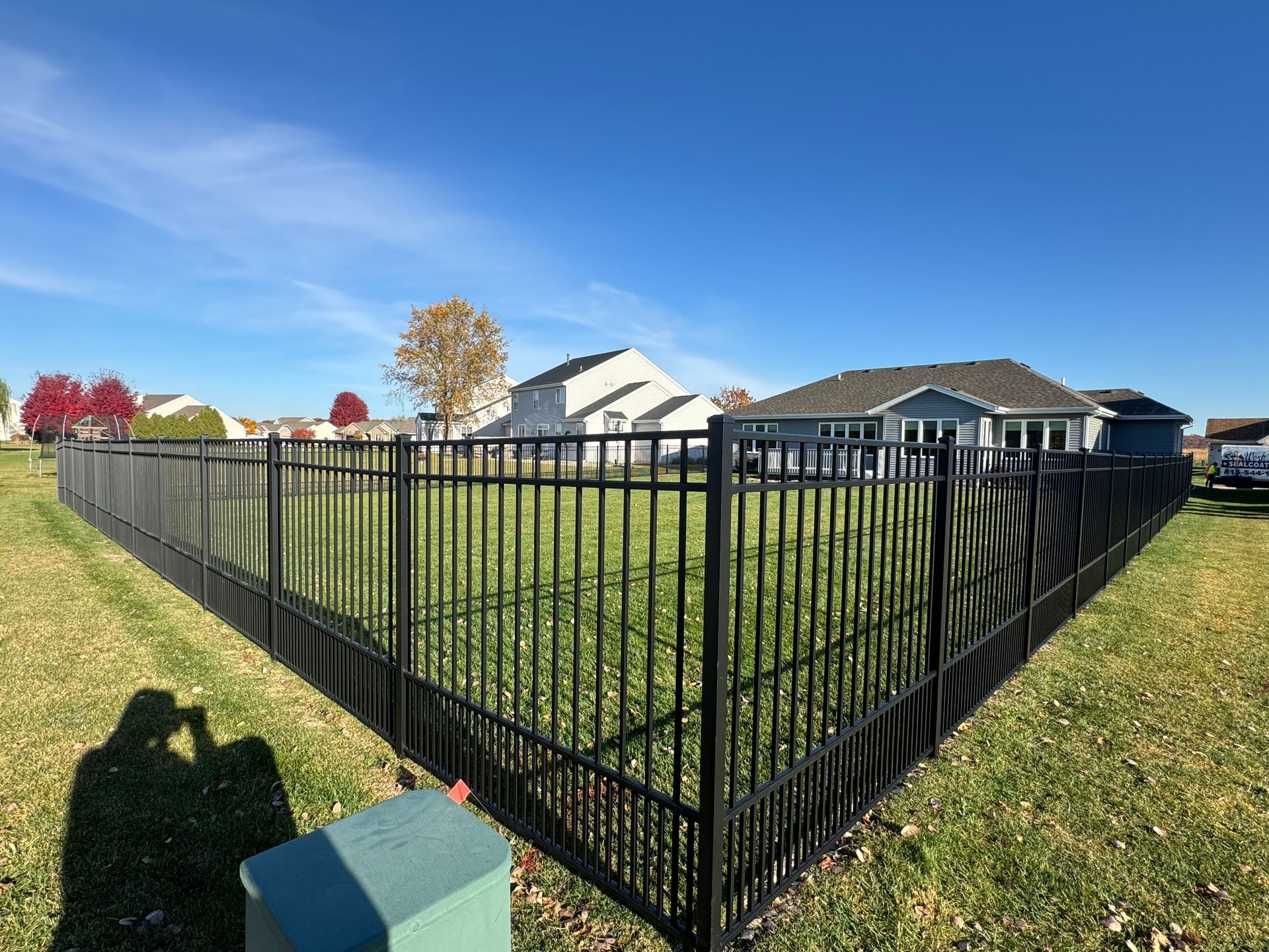 A black fence surrounds a lush green field in front of a house.