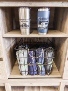 Two stainless steel tumblers are sitting on a wooden shelf next to a basket of bags.