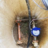 A water meter is sitting in the middle of a hole in the ground.