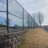 A chain link fence surrounds a tennis court.