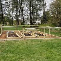 A wooden fence surrounds a garden with lots of raised beds.