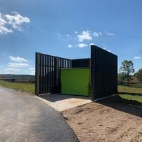 A green trash can is sitting next to a road.