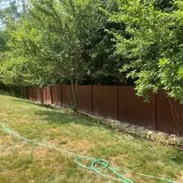 A red fence surrounds a lush green yard with trees and a hose.