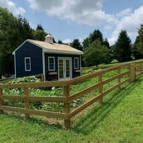 A blue house is behind a wooden fence in a grassy field.