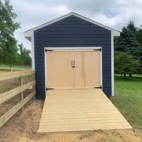 A blue garage with wooden doors and a ramp leading to it.