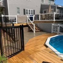 A wooden deck with stairs leading to a swimming pool in front of a house.