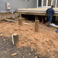 A man is standing in the dirt next to a wooden deck.