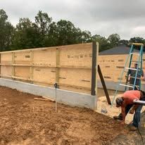 A man is working on a wooden wall in a dirt field.