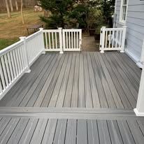 A gray deck with a white railing and stairs leading up to it.